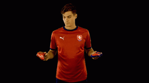 a man in a red puma shirt holds two soccer balls