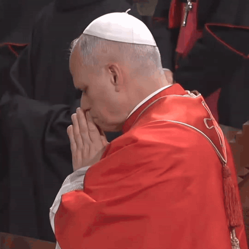 A Man In A Red Robe And White Hat Prays GIF