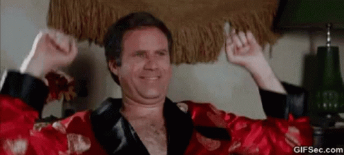A Man In A Red Robe Is Holding A Cigarette In His Hand And Smiling . GIF