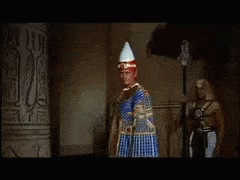 A Man In A Red Robe Is Standing Next To A Woman In A Gold Dress GIF