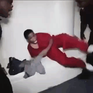 A Man In A Red Scrub Suit Is Laying On A Bed Being Thrown By A Group Of People . GIF