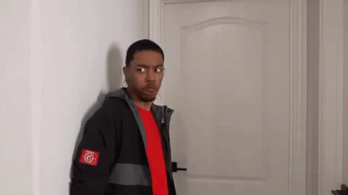 A Man In A Red Shirt And A Black Jacket Is Standing In Front Of A Door . GIF
