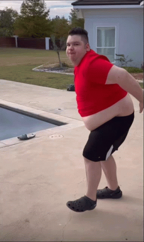 A Man In A Red Shirt And Black Shorts Is Standing In Front Of A Swimming Pool GIF