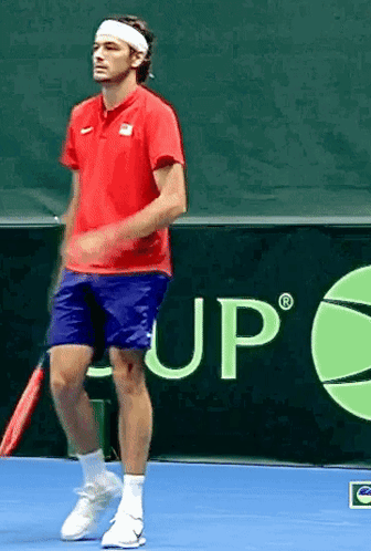 A Man In A Red Shirt And Blue Shorts Is Holding A Tennis Racquet On A Tennis Court GIF