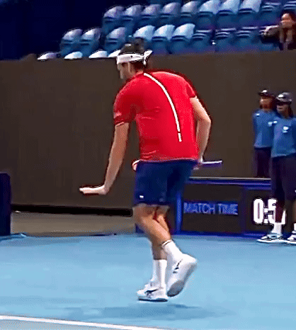 A Man In A Red Shirt And Blue Shorts Is Jumping On A Tennis Court . GIF