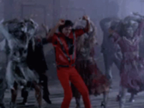 A Man In A Red Shirt And Red Pants Is Dancing In Front Of A Crowd Of Zombies . GIF