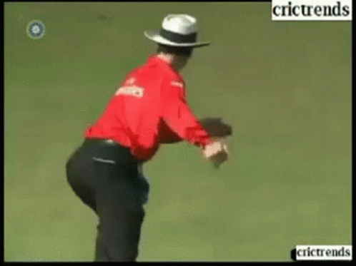 A Man In A Red Shirt And White Hat Is Standing On A Field With The Words Crictrends Below Him GIF