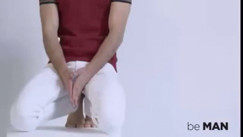 A Man In A Red Shirt And White Pants Is Sitting On A Chair With His Hands On His Lap . GIF