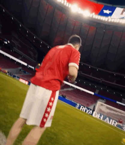 A Man In A Red Shirt And White Shorts Stands On A Soccer Field With An Ad For Riyadh Air Behind Him GIF