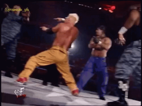 A Man In A Red Shirt And Yellow Pants Is Dancing On A Stage With Wrestlers In The Background GIF