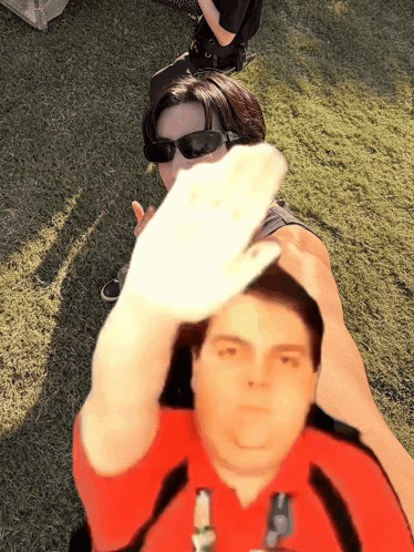 a man in a red shirt holds up his hand in front of a woman in sunglasses