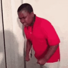 A Man In A Red Shirt Is Crying While Standing Next To A Door . GIF
