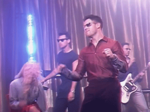 A Man In A Red Shirt Is Dancing On A Stage With A Guitar Player . GIF
