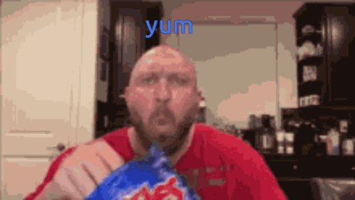 A Man In A Red Shirt Is Eating A Bag Of Potato Chips And The Word Yum Is Above Him GIF