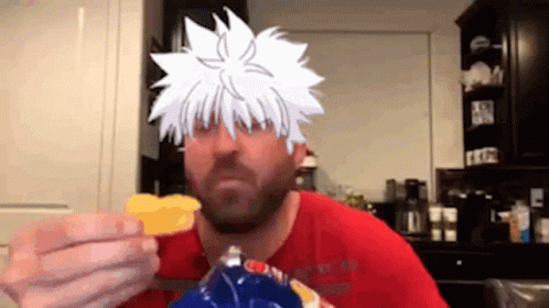 A Man In A Red Shirt Is Eating Chips With A Cartoon Character On His Face . GIF