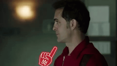 A Man In A Red Shirt Is Holding A Foam Finger In His Right Hand . GIF