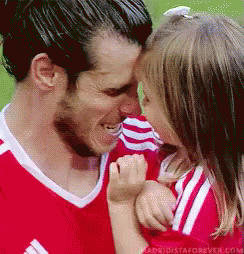 A Man In A Red Shirt Is Holding A Little Girl In His Arms And Kissing Her On The Forehead . GIF