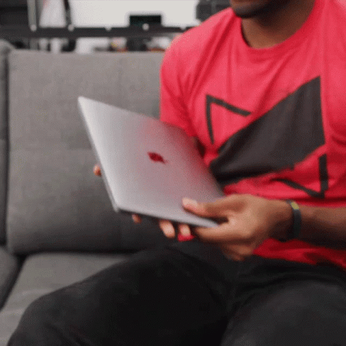 A Man In A Red Shirt Is Holding A Silver Apple Laptop GIF