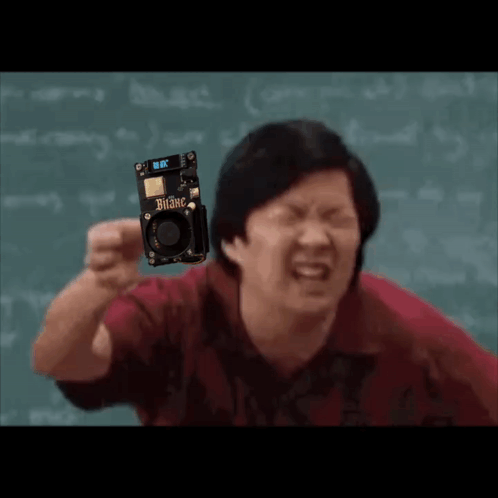 A Man In A Red Shirt Is Holding A Small Electronic Device . GIF