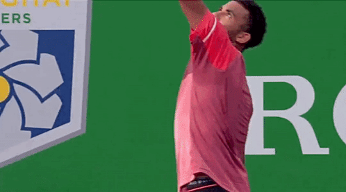 A Man In A Red Shirt Is Holding A Tennis Racquet In Front Of A Red Bull Logo GIF