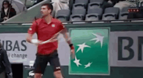 A Man In A Red Shirt Is Holding A Tennis Racquet In Front Of An Bnp Logo GIF