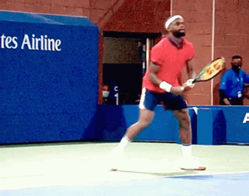 a man in a red shirt is holding a tennis racquet on a tennis court in front of a tes airline sign