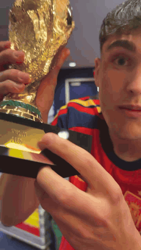 A Man In A Red Shirt Is Holding A Trophy That Says ' Fifa World Cup ' On It GIF