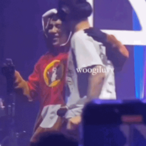 A Man In A Red Shirt Is Hugging Another Man In A White Shirt On Stage . GIF