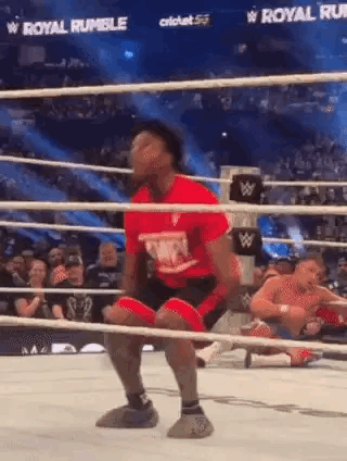 A Man In A Red Shirt Is Kneeling In A Wrestling Ring While Another Man Is Laying On The Ground . GIF