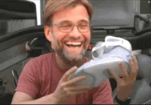A Man In A Red Shirt Is Laughing While Holding A White Shoe GIF