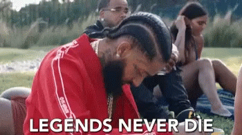 A Man In A Red Shirt Is Laying On The Grass With The Words `` Legends Never Die '' Written Above Him . GIF