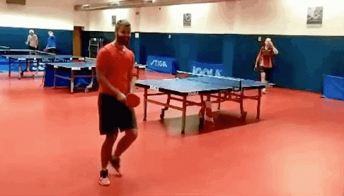 A Man In A Red Shirt Is Playing Ping Pong In A Room With Ping Pong Tables By Joola GIF