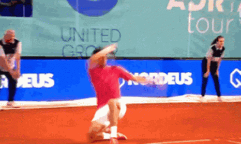 A Man In A Red Shirt Is Playing Tennis In Front Of A Banner That Says United Group GIF