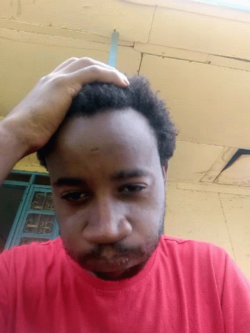 A Man In A Red Shirt Is Scratching His Head With His Hand GIF