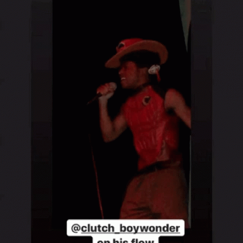 A Man In A Red Shirt Is Singing Into A Microphone . GIF