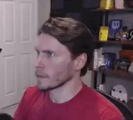 A Man In A Red Shirt Is Sitting In A Chair In Front Of A Computer . GIF