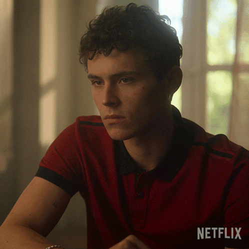A Man In A Red Shirt Is Sitting In Front Of A Window With A Netflix Logo Behind Him GIF