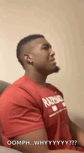 A Man In A Red Shirt Is Sitting On A Couch And Making A Funny Face . GIF