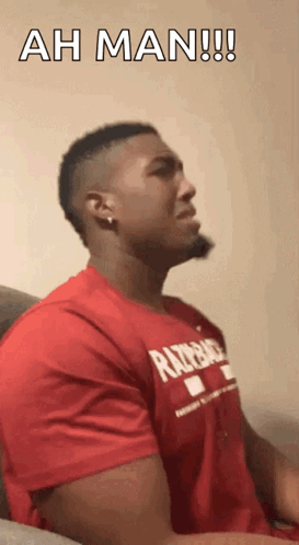 A Man In A Red Shirt Is Sitting On A Couch And Says Ah Man !! GIF