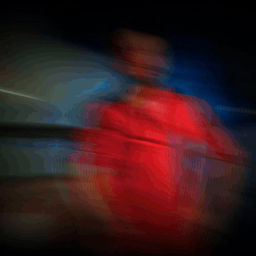 A Man In A Red Shirt Is Standing In A Dark Room With Smoke Behind Him GIF