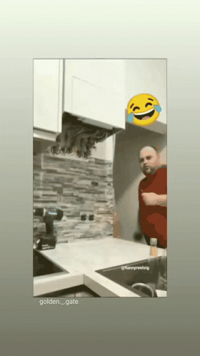 A Man In A Red Shirt Is Standing In A Kitchen With A Yellow Smiley Face Behind Him GIF