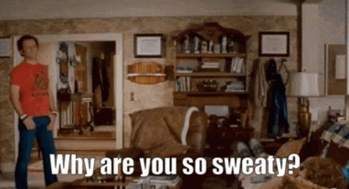 A Man In A Red Shirt Is Standing In A Living Room Asking Why Are You So Sweaty . GIF