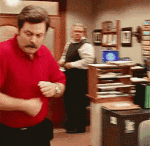 A Man In A Red Shirt Is Standing In A Room GIF
