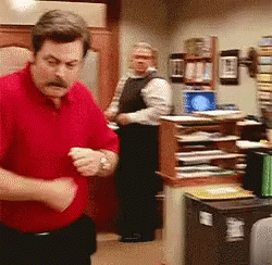 A Man In A Red Shirt Is Standing In A Room With Other Men GIF