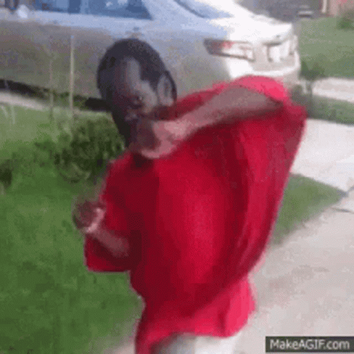 A Man In A Red Shirt Is Standing In Front Of A Car . GIF
