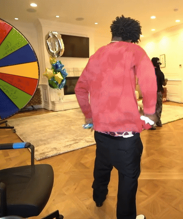 A Man In A Red Shirt Is Standing In Front Of A Colorful Spinning Wheel GIF