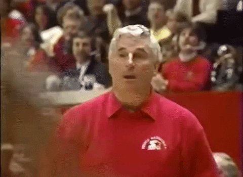A Man In A Red Shirt Is Standing In Front Of A Crowd In A Stadium . GIF