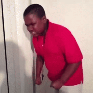 A Man In A Red Shirt Is Standing In Front Of A Door And Making A Funny Face . GIF