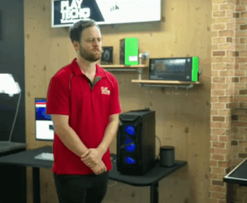 A Man In A Red Shirt Is Standing In Front Of A Sign That Says Play Hard Tech GIF