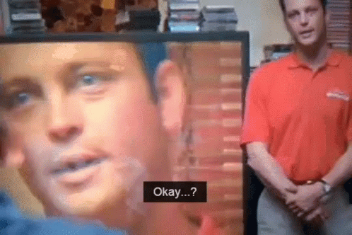 A Man In A Red Shirt Is Standing In Front Of A Tv Screen That Says Okay GIF
